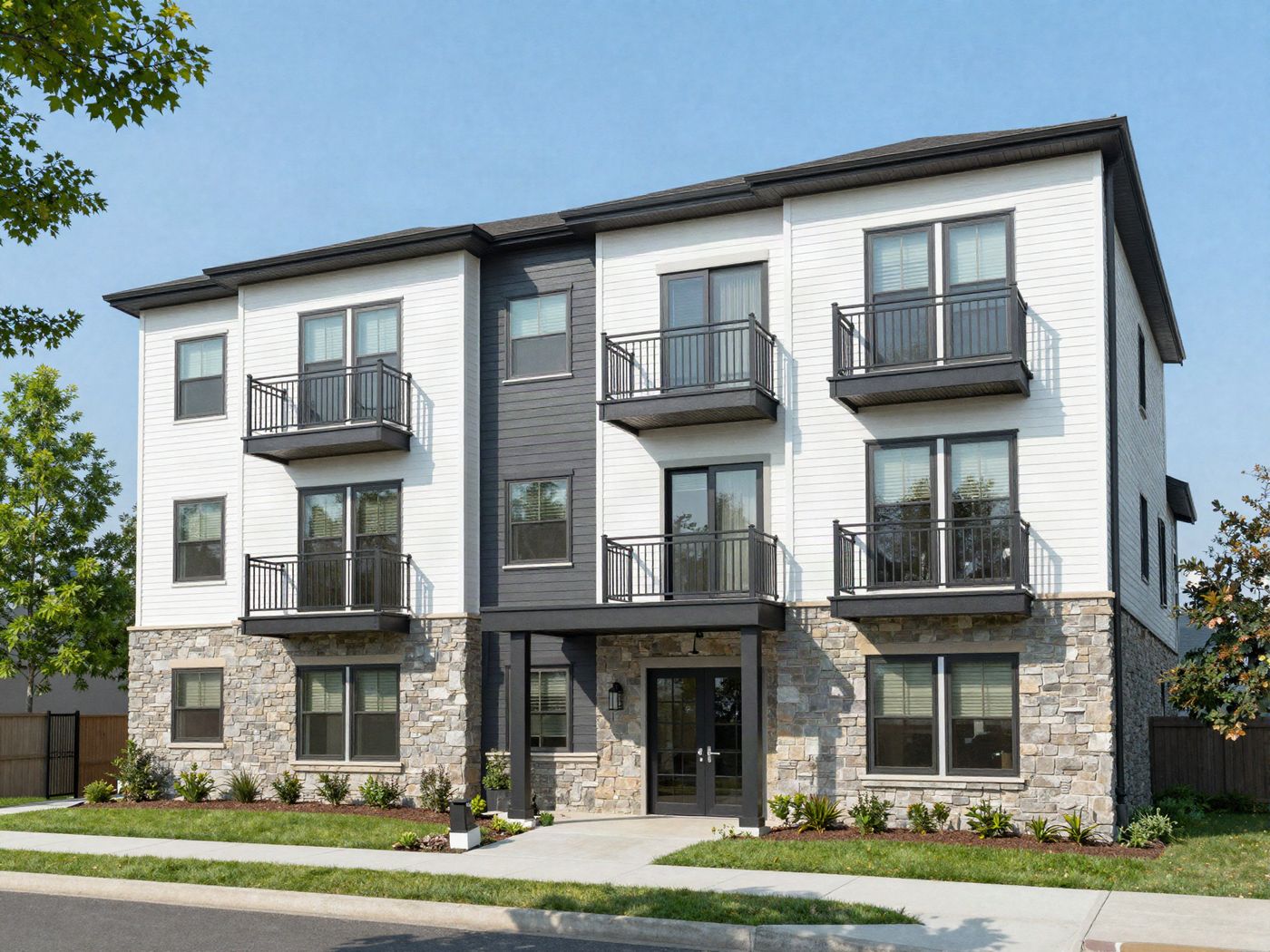 A three-story building with white siding, a stone base and black balconies